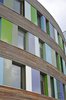 Curved office facade of bands of larch wood, glass, and color panels; raking view showing inset windows; the reveals (30 cm) of the colored blocks are also colored
