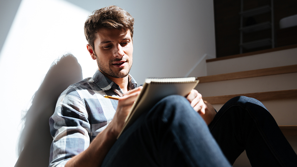 Man sitting on stairs at home and writing in notepad