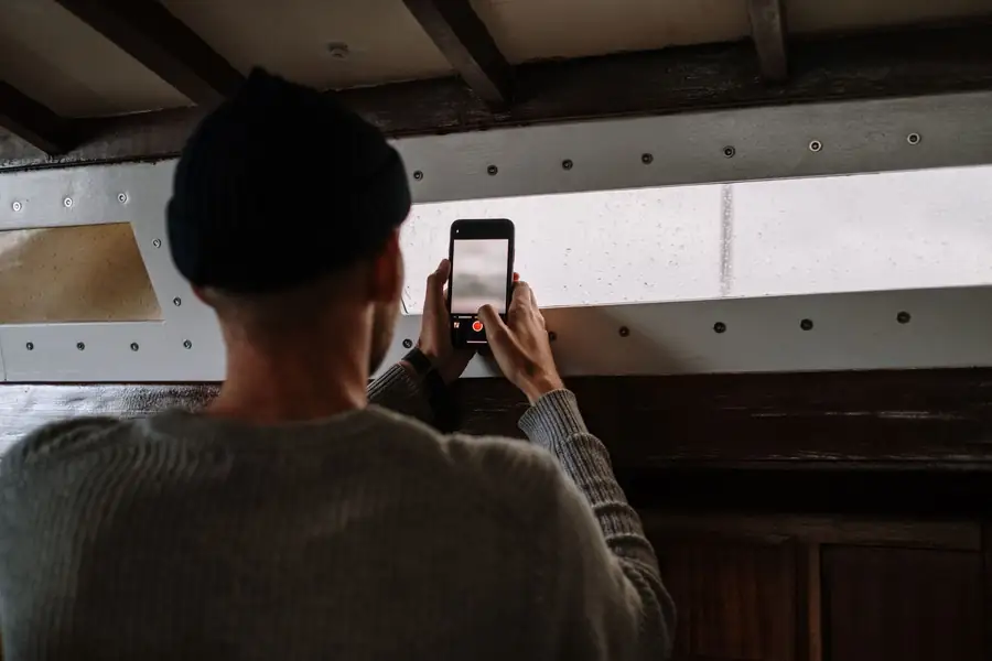 Homem de suéter cinza tirando uma foto com o smartphone dentro de uma sala de madeira Homem de suéter cinza tirando uma foto com o smartphone dentro de uma sala de madeira