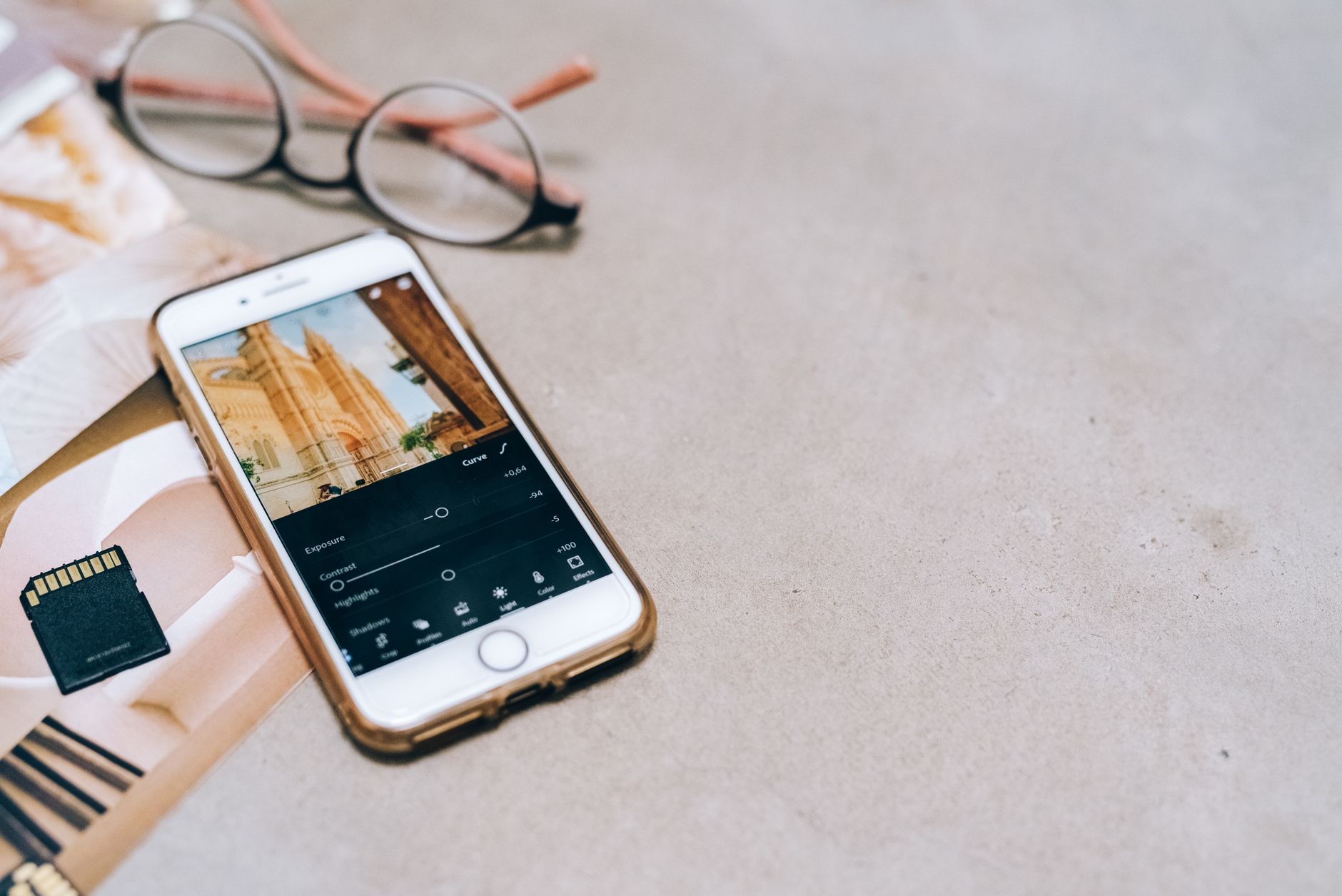 Smartphone displaying a photo editing app, next to a memory card and glasses on a table.