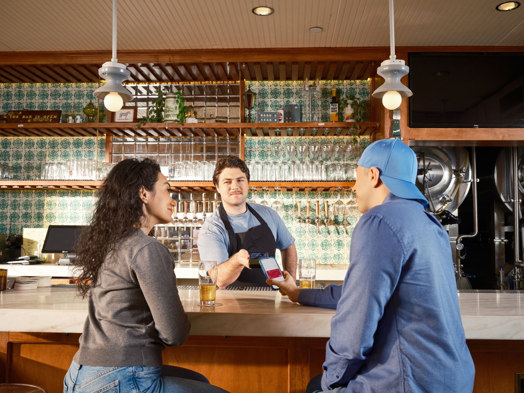 Android puro, One UI ou HyperOS: qual interface escolher A couple uses mobile payment at a trendy bar with a bartender assisting.