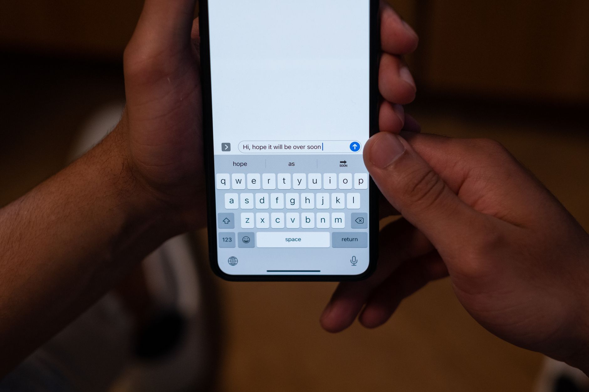 Close-up of hands texting on a smartphone indoors with a hopeful message on screen.