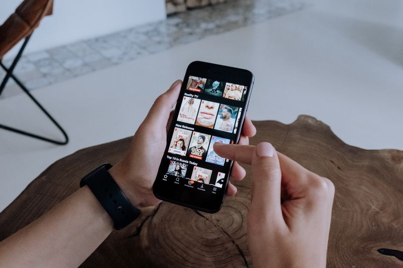 Armazenamento do sistema cheio: o que é e como reduzir A person using a smartphone to explore and select shows on a streaming platform indoors.