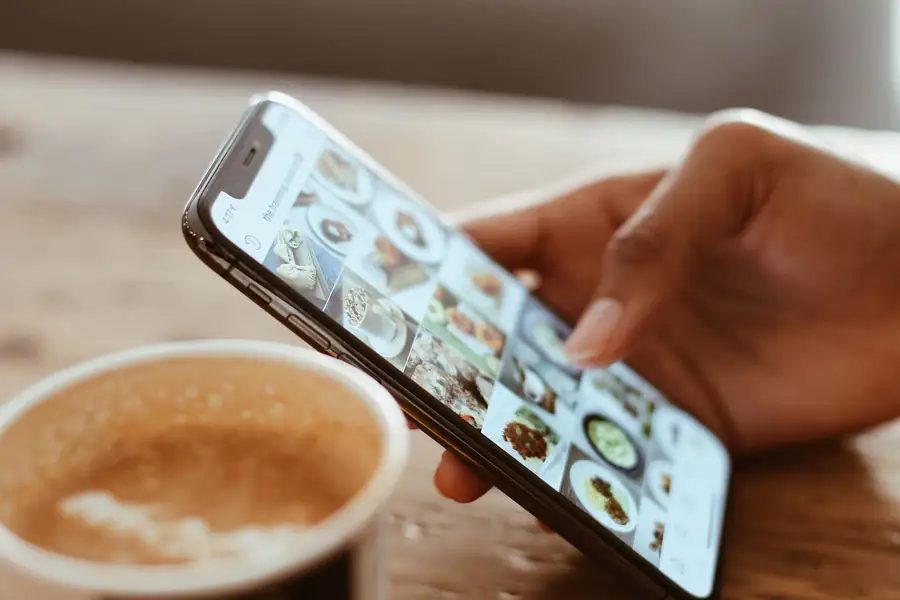 Mão navegando por fotos no celular ao lado de uma xícara de café Mão navegando por fotos no celular ao lado de uma xícara de café