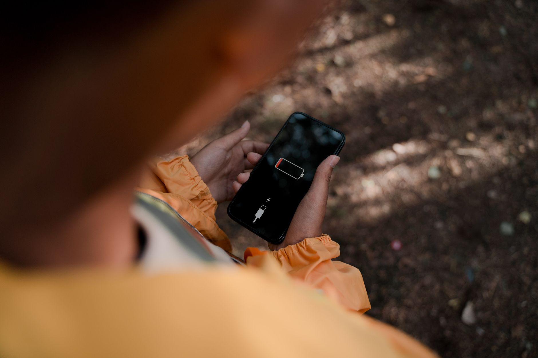 Bateria de silício-carbono: o que muda no celular Teenage boy holds a smartphone displaying low battery outdoors in a forest.