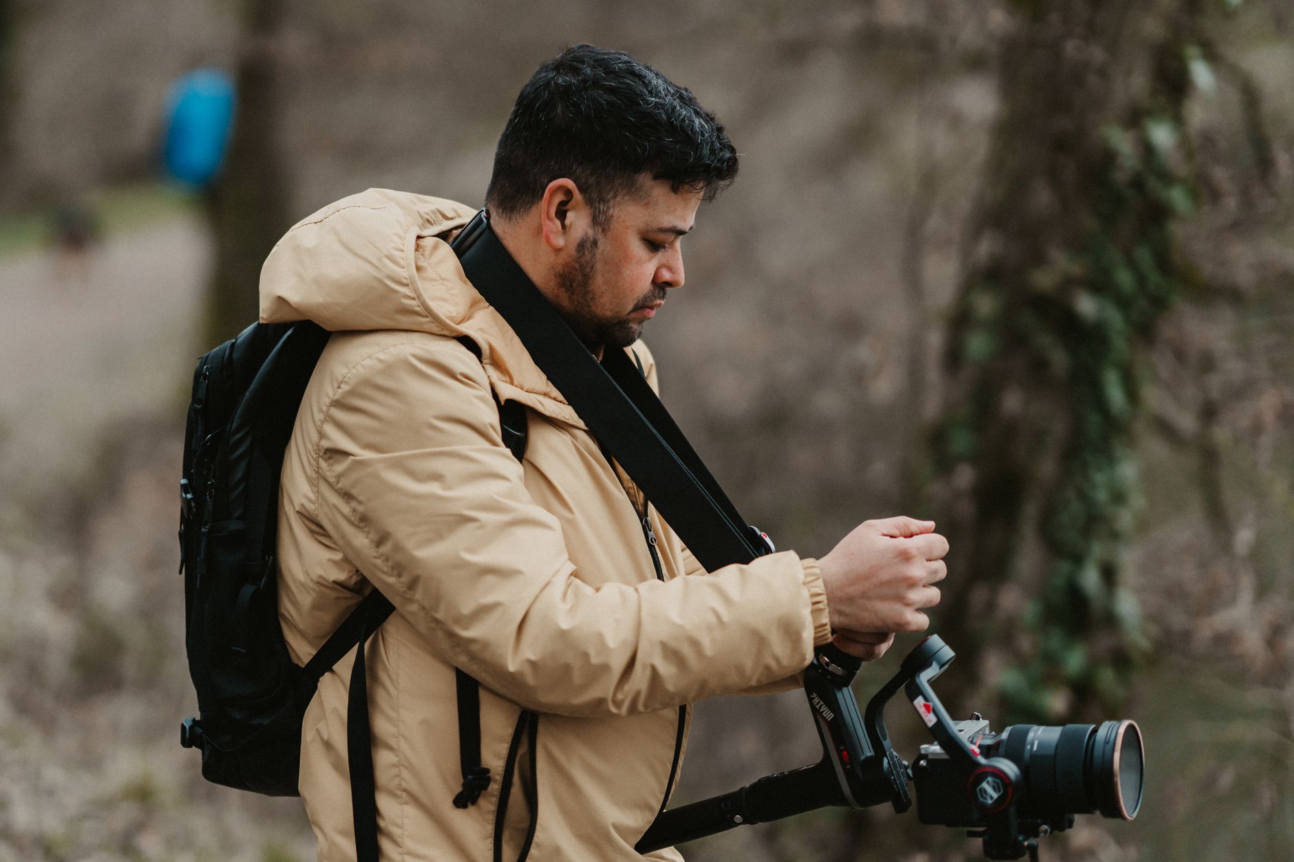 Como escolher entre câmera de celular e câmera profissional A professional photographer in a beige jacket adjusting his camera in a natural outdoor setting.
