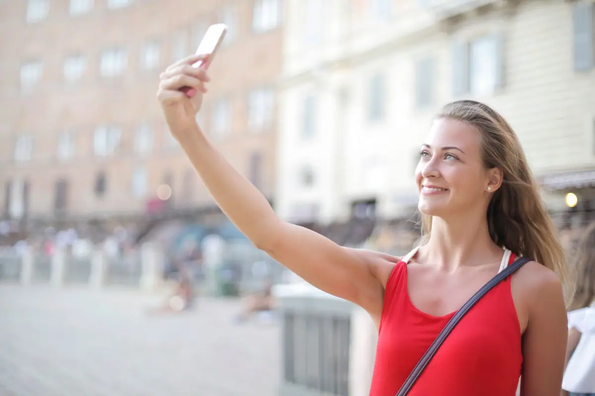 Mulher sorrindo ao tirar uma selfie com o celular em uma rua