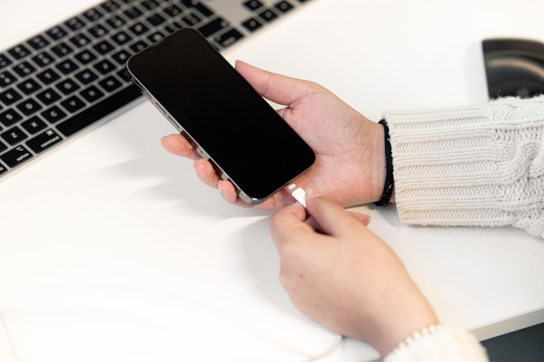 Pessoa conectando um carregador a um celular sobre uma mesa