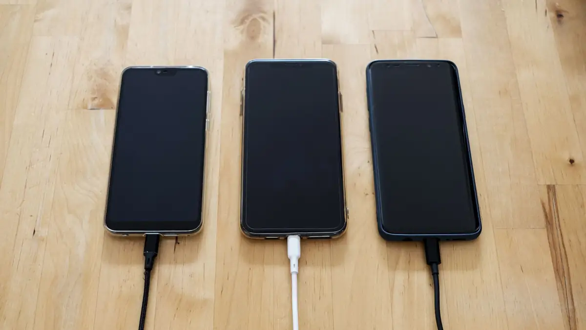 Três celulares conectados a carregadores sobre uma superfície de madeira