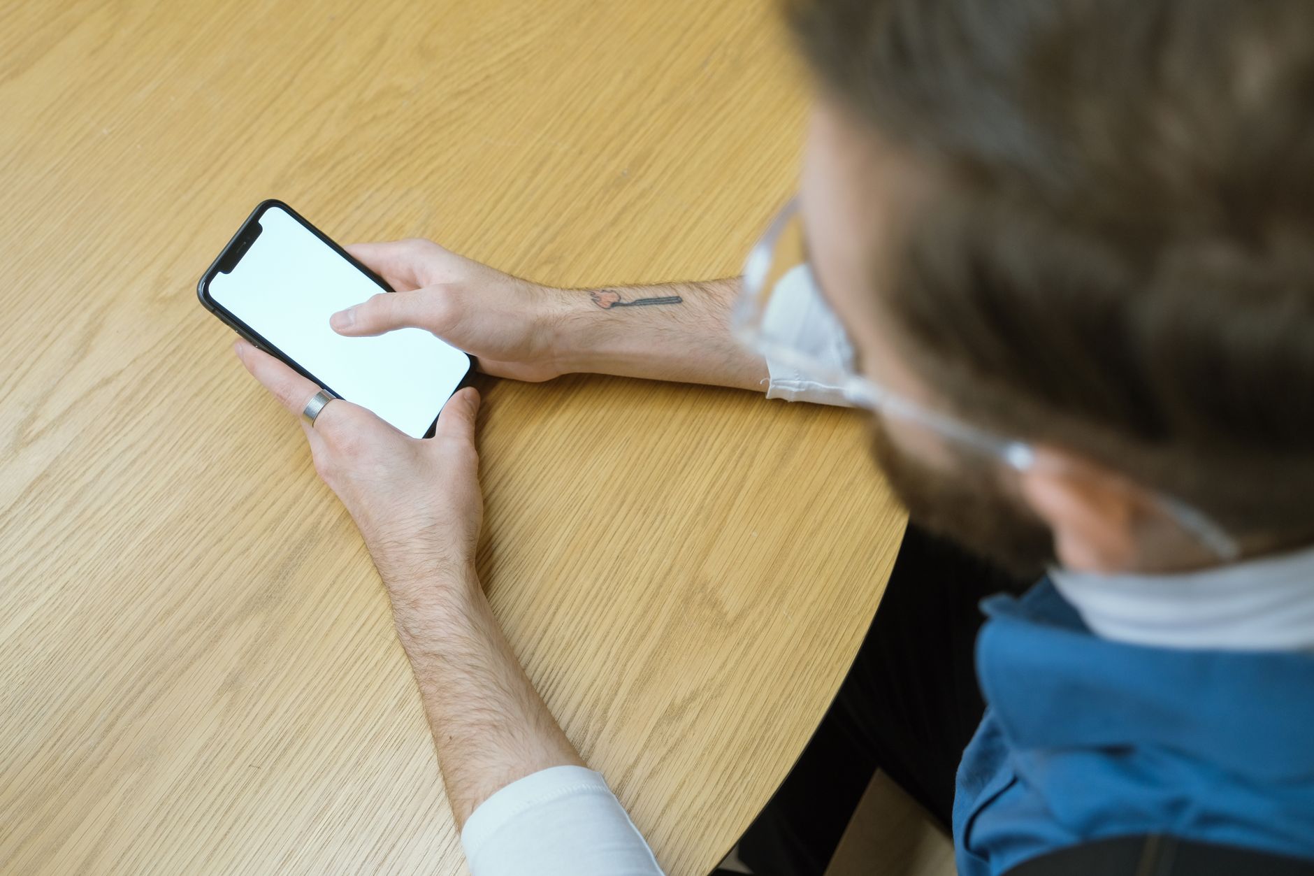 Overhead view of person holding smartphone with blank screen at a wooden table.