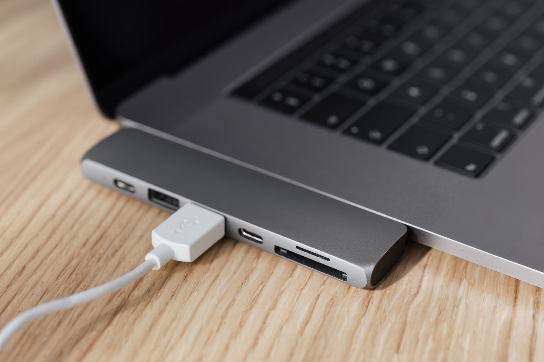 Como escolher um celular com entrada para cartão SD High angle of modern space silver laptop with USB type c multiport hub with plugged white cable placed on wooden table