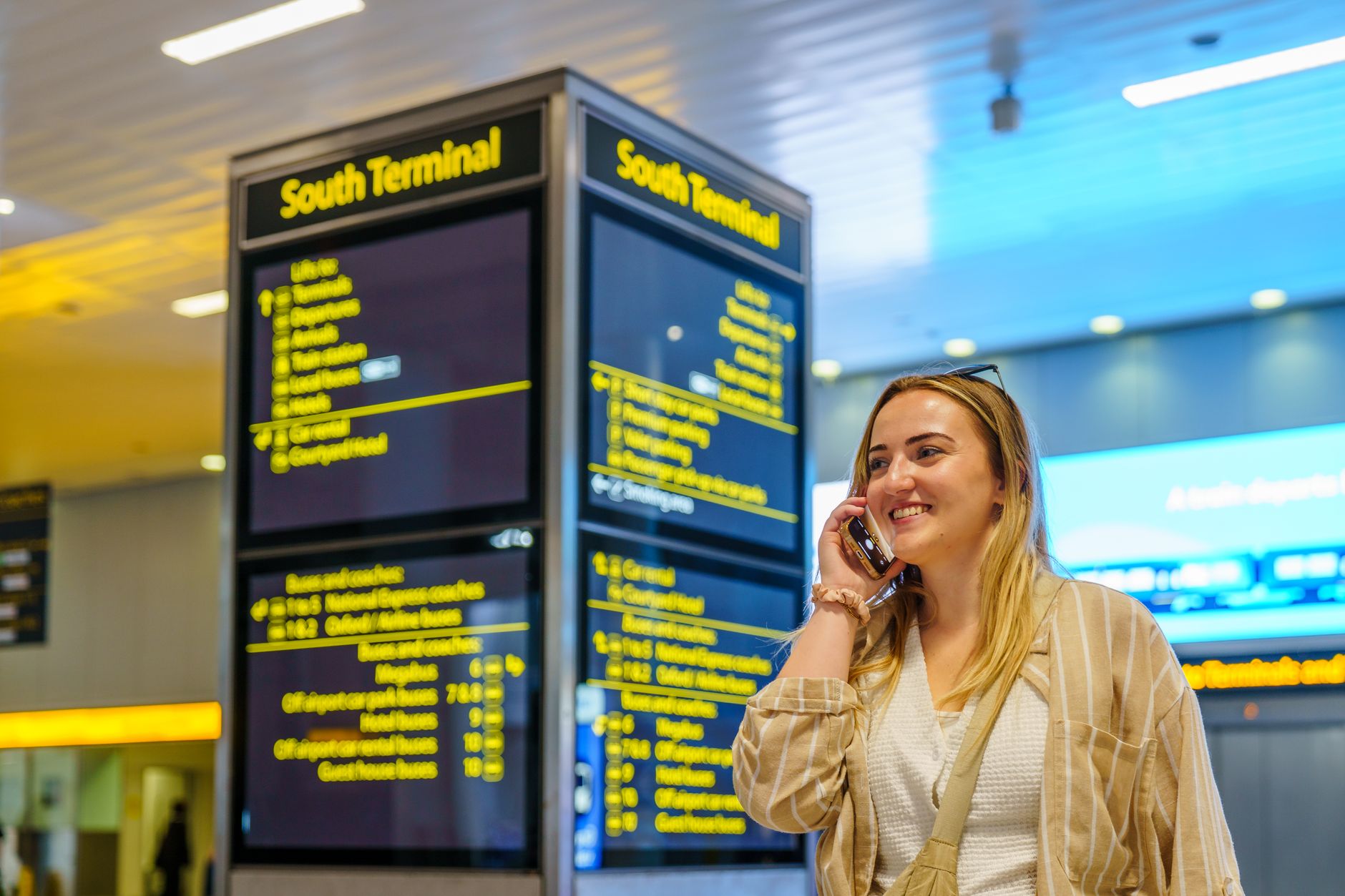 Celular importado vale a pena? O que você perde Smiling woman on phone in South Terminal of Gatwick Airport, Horley, enjoying her travel experience.