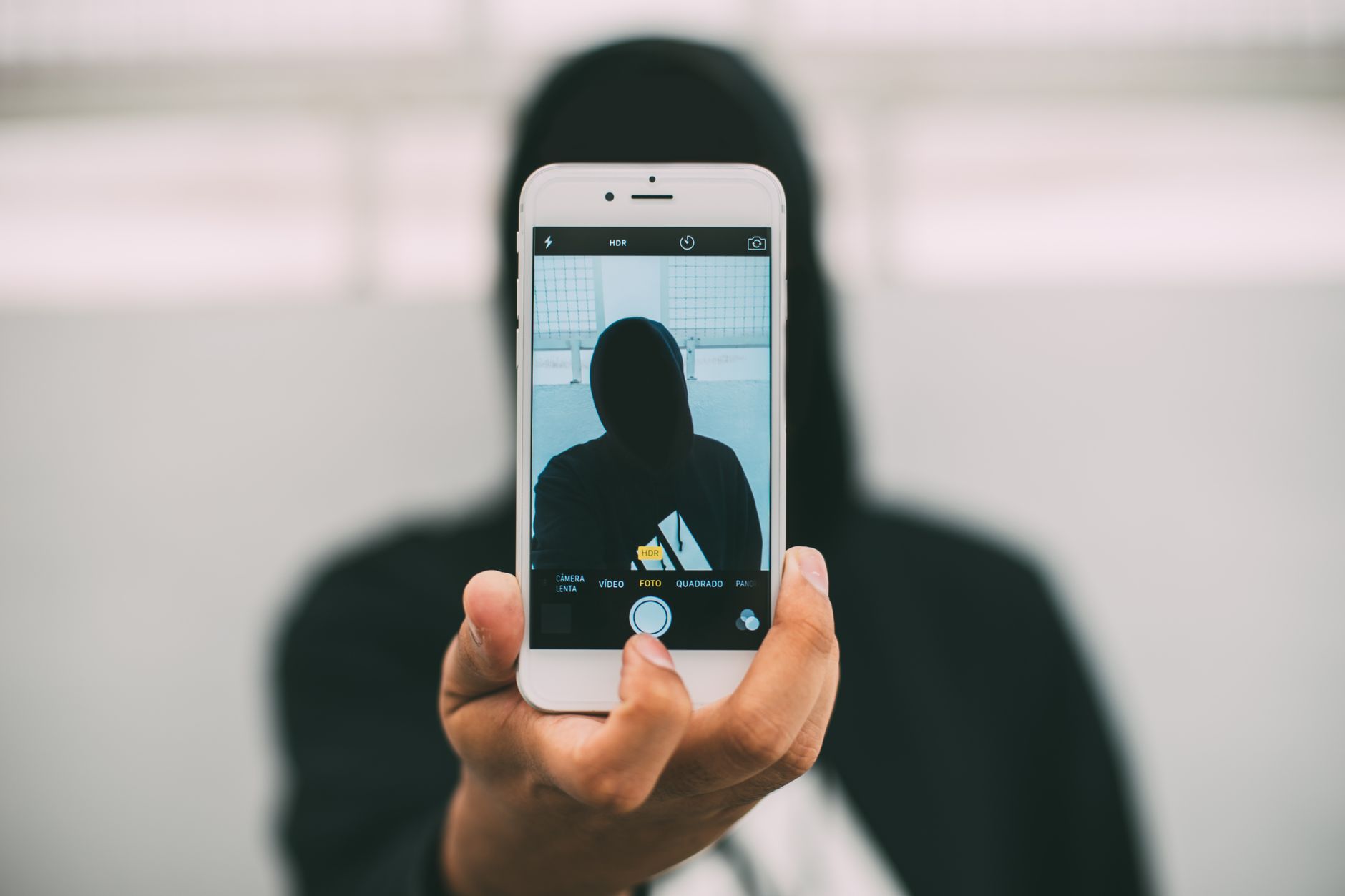 Intermediário ou top de linha: vale pagar a diferença? A person in a hoodie takes a mysterious selfie with a smartphone.