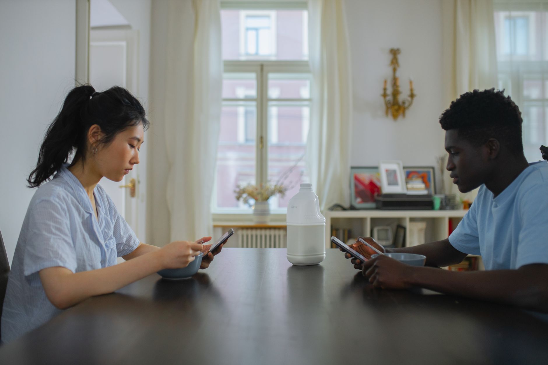 Celular caiu na água: o que fazer e o que evitar A couple engaging with their phones over breakfast, highlighting modern technology use in everyday life.