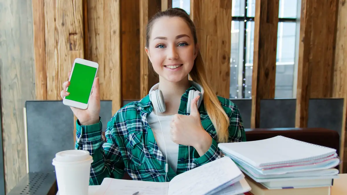 Jovem estudando com um smartphone ao lado de livros