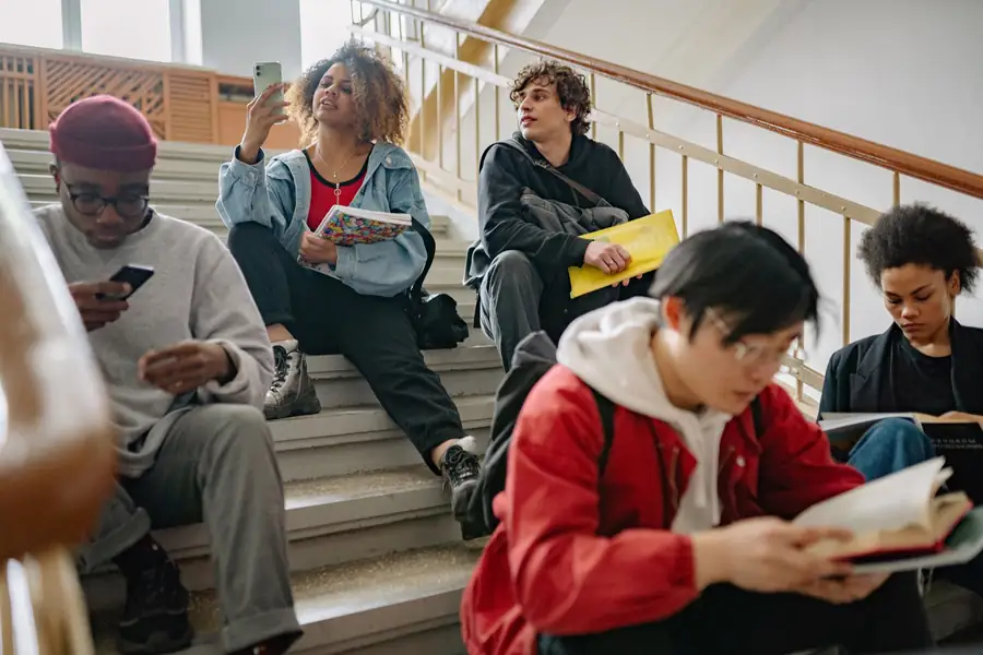 Estudantes sentados em escadaria de universidade usando celulares Estudantes sentados em escadaria de universidade usando celulares