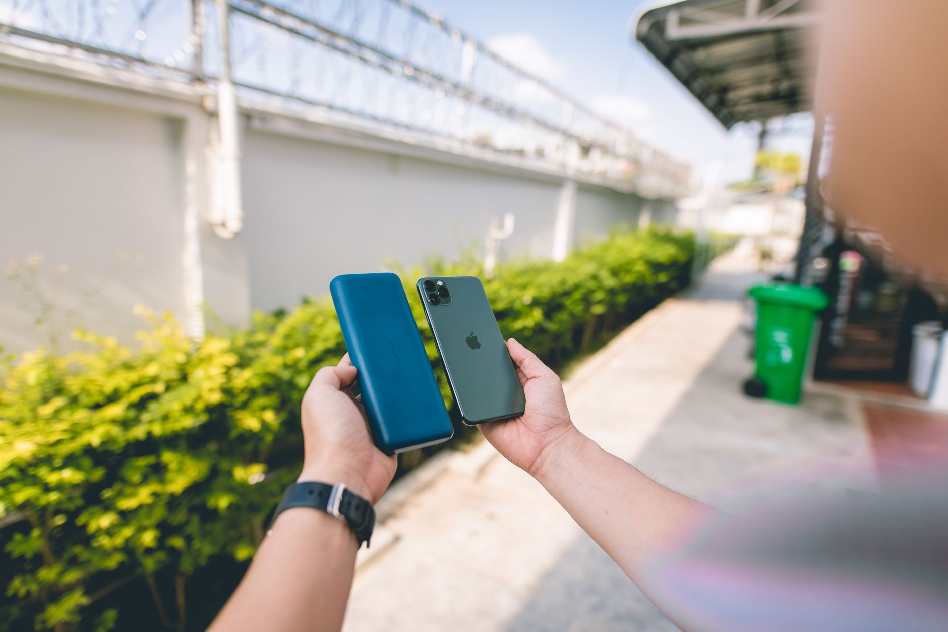 Celular usado: 12 testes antes de comprar Close-up of a smartphone and power bank held in hands in an outdoor setting.