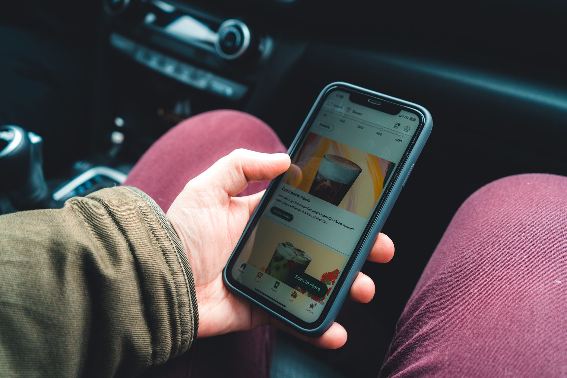 Modo escuro: como ativar e se economiza bateria Hand holding smartphone showing a coffee app interface in a car interior setting.
