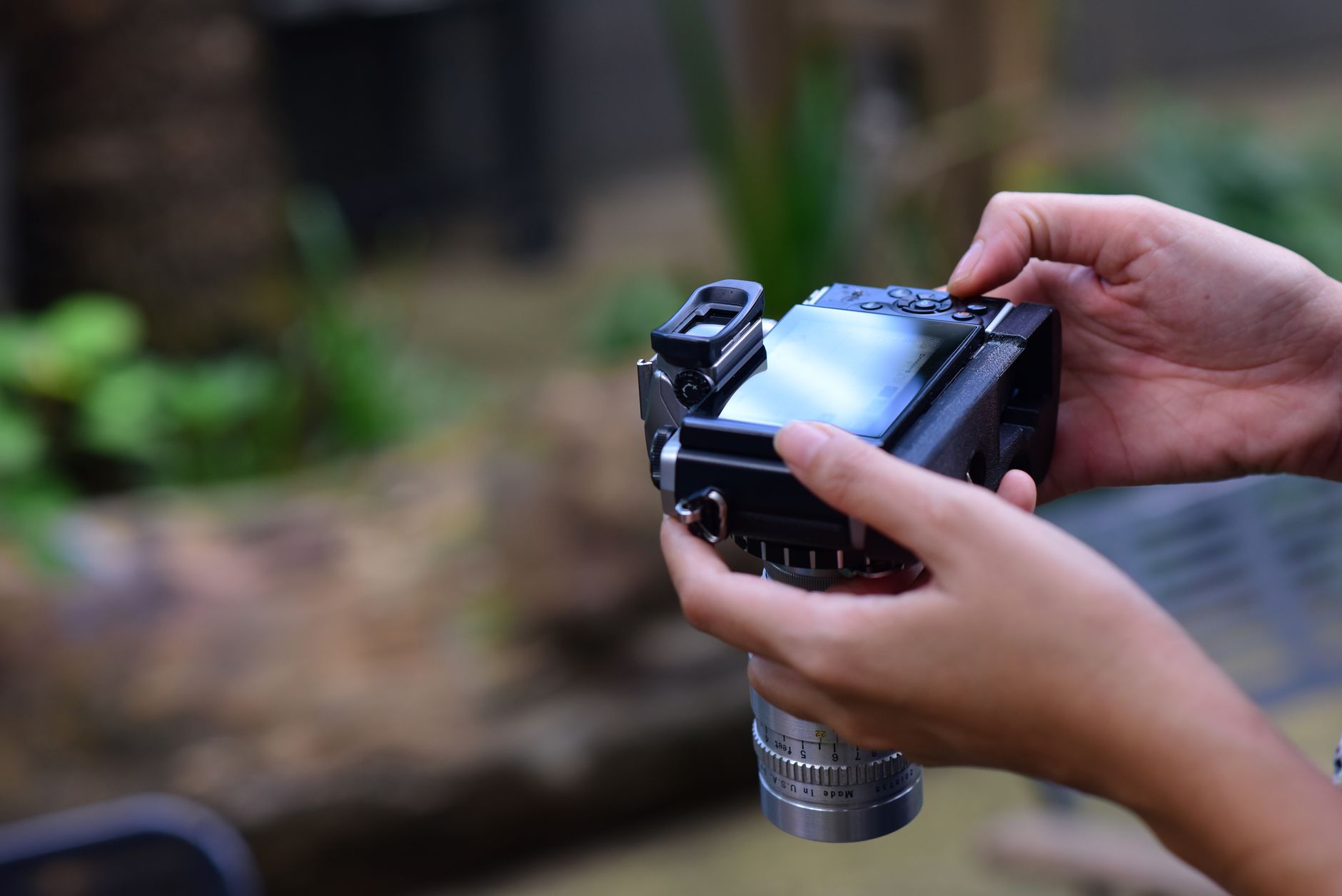 Como ativar o roaming internacional sem pagar a mais A photographer holds and adjusts a digital camera outdoors, preparing to take a photo.