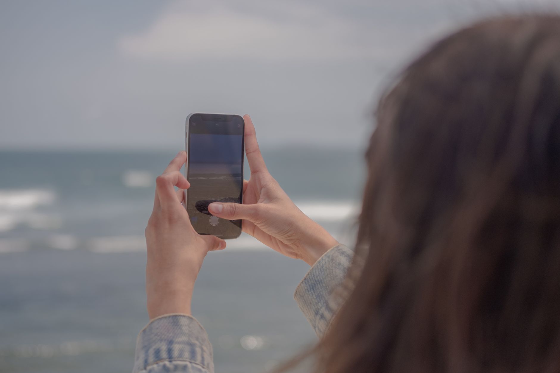 Pessoa segurando um celular com as duas mãos enquanto grava uma paisagem ao ar livre.