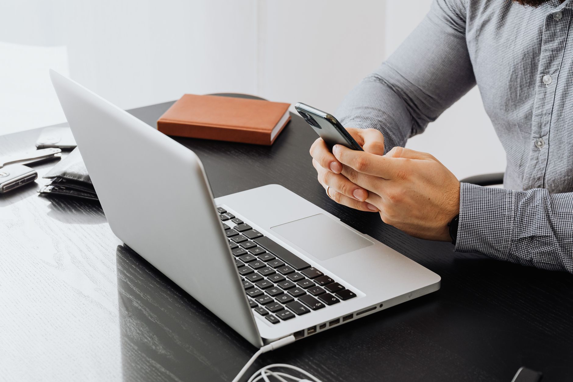 Como recuperar fotos apagadas do celular An adult using a smartphone at an office desk with a laptop for work.