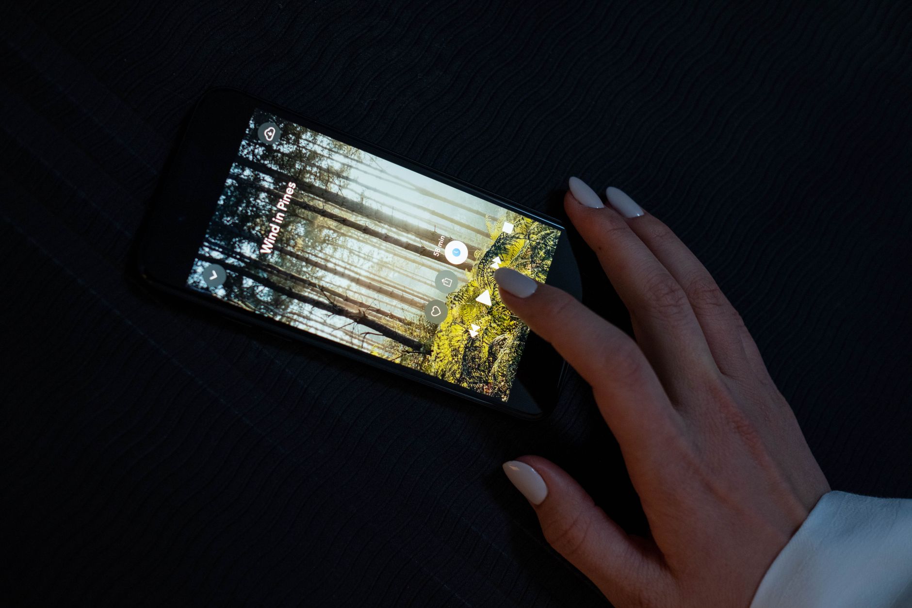 Como tirar print de tela em qualquer celular A hand interacting with a smartphone displaying a forest-themed app on a dark surface.