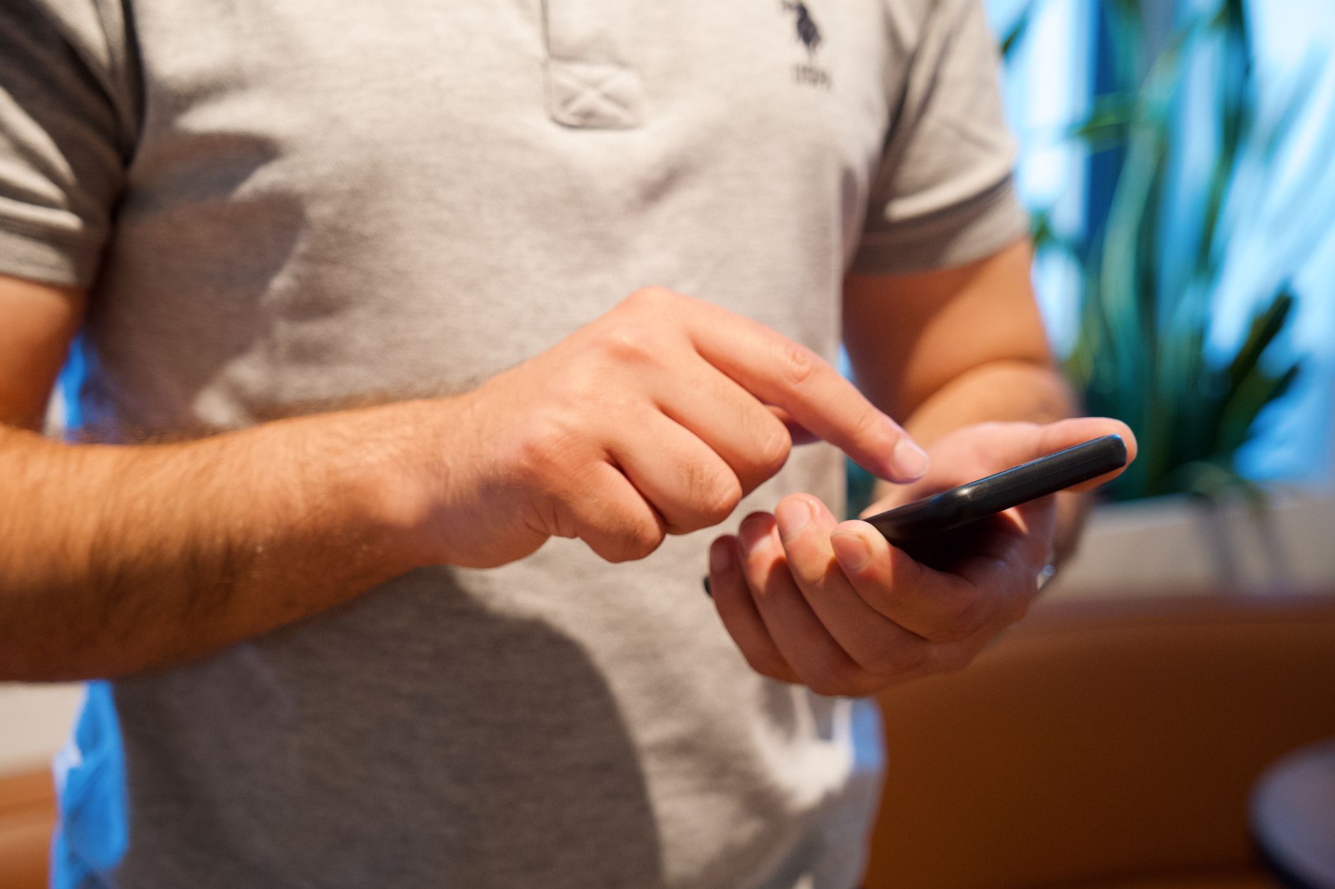 Buscar iPhone: como localizar, bloquear ou apagar Adult male using smartphone in a bright indoor setting, focusing on the device and interaction.