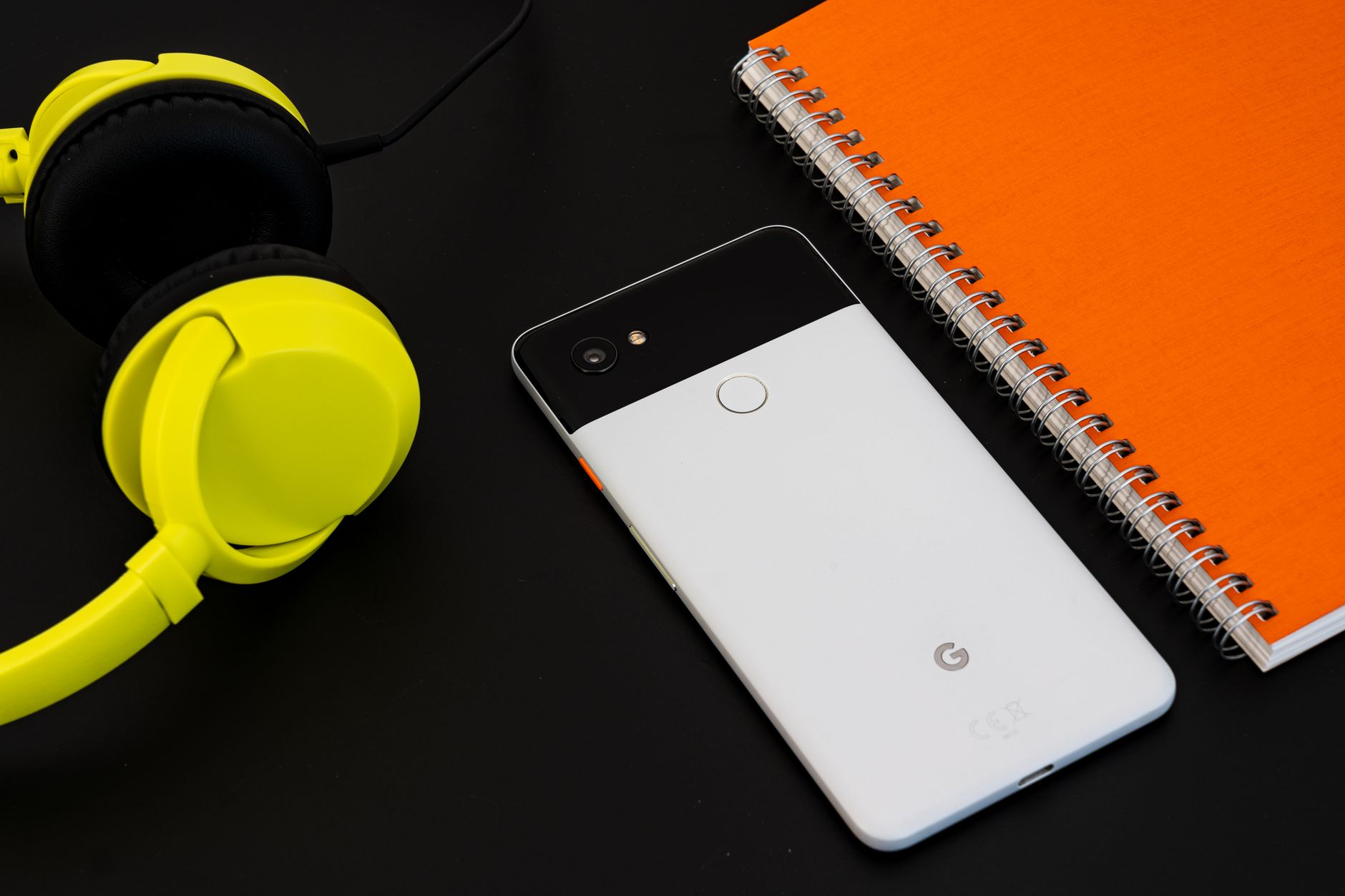 Como usar dois WhatsApp no mesmo celular A vibrant flat lay image of a smartphone, yellow headphones, and an orange spiral notebook on a desk.