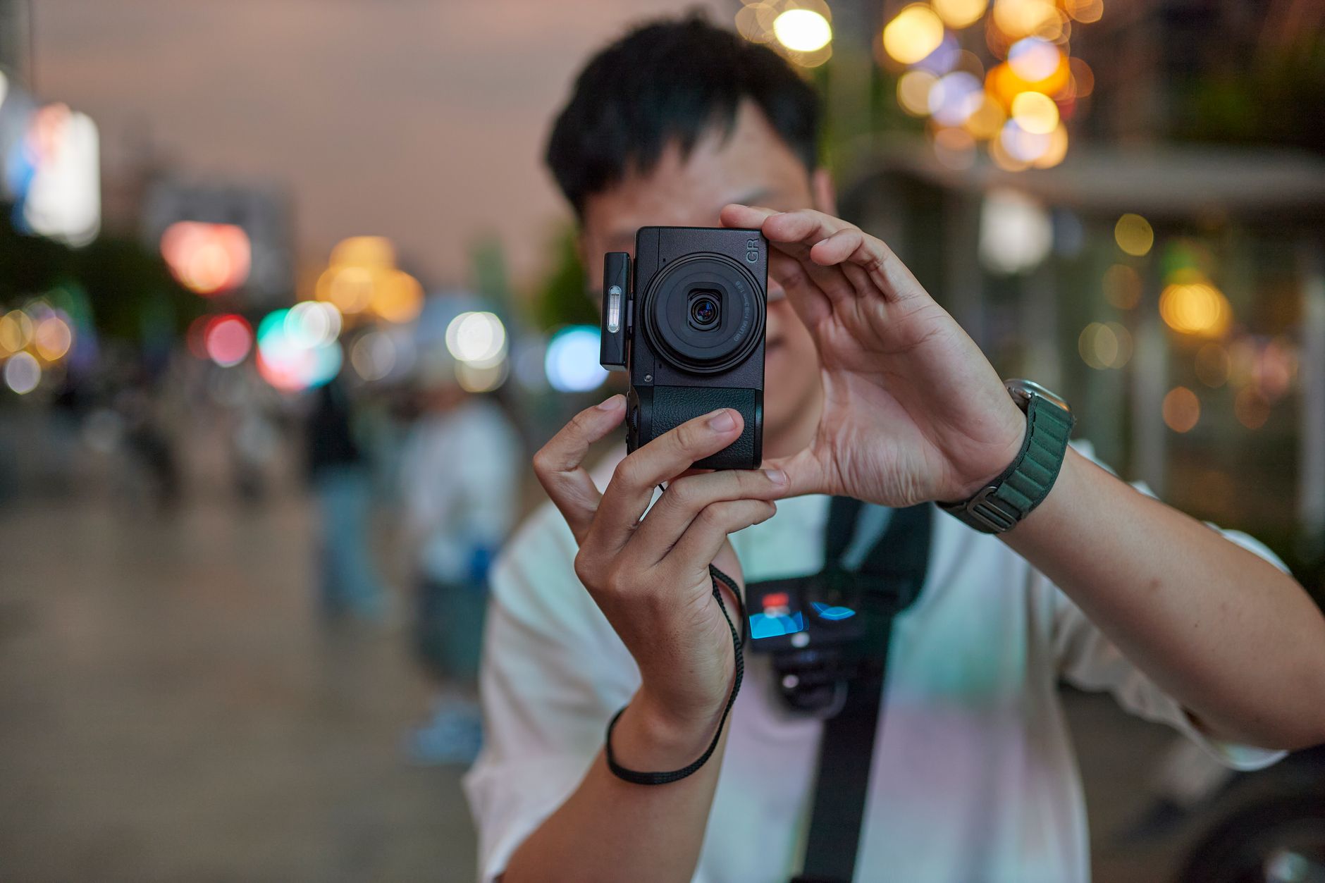 Pessoa fotografando uma rua iluminada à noite com um celular apoiado nas mãos