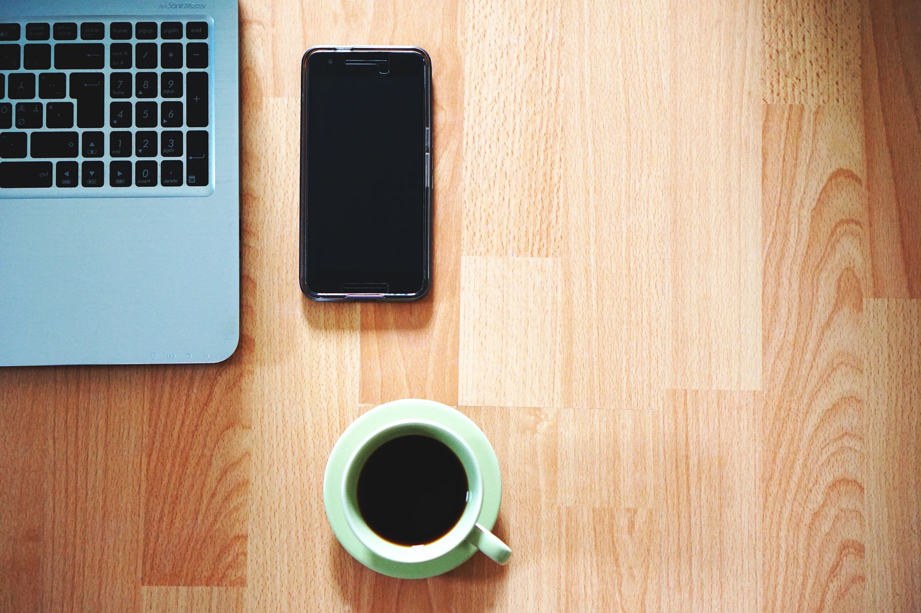 Como ver a saúde da bateria do iPhone e quando trocar A tidy workspace with a laptop, smartphone, and coffee cup on a wooden desk.