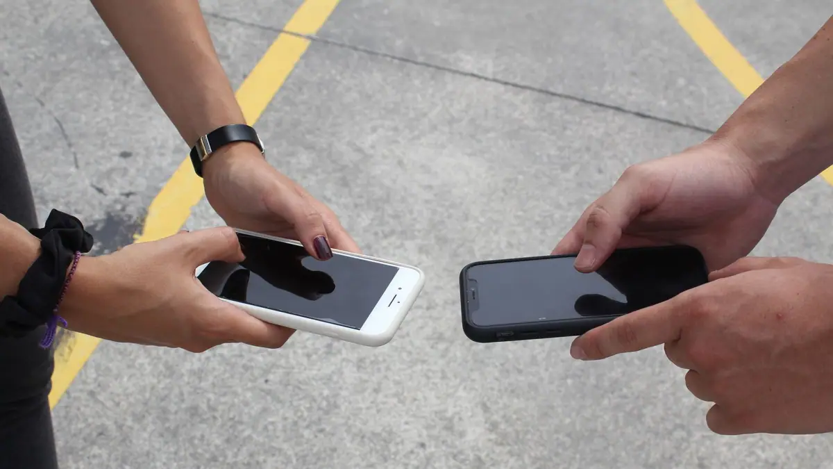 Duas pessoas trocando smartphones ao ar livre