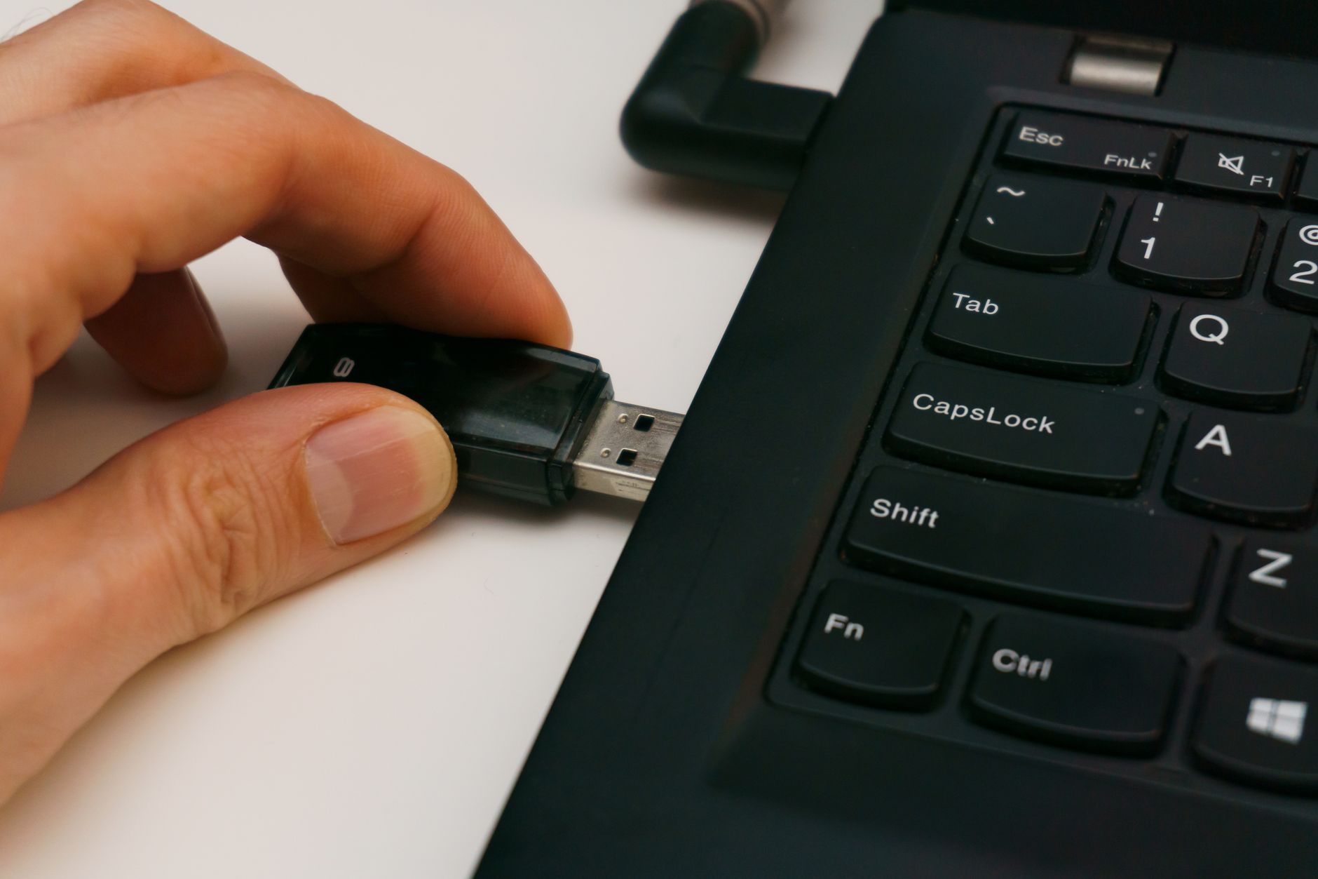 Dual SIM: como funciona e quais são os tipos no celular Close-up of a USB pen drive being inserted into a laptop USB port on a white surface.