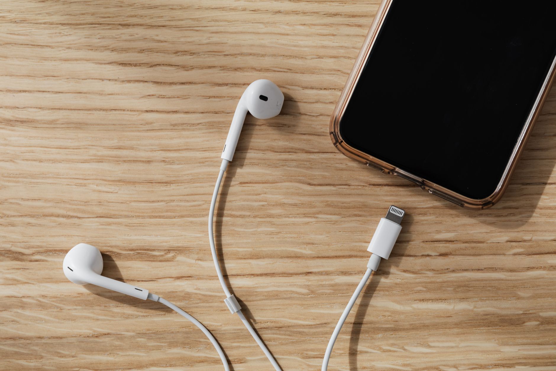 Pessoa conectando um fone com fio a um celular sobre uma mesa