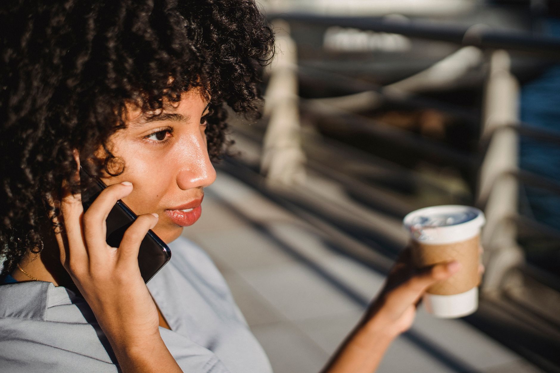 Galaxy AI: o que faz e em quais celulares funciona African American woman with curly hair having a phone conversation while holding a coffee cup.