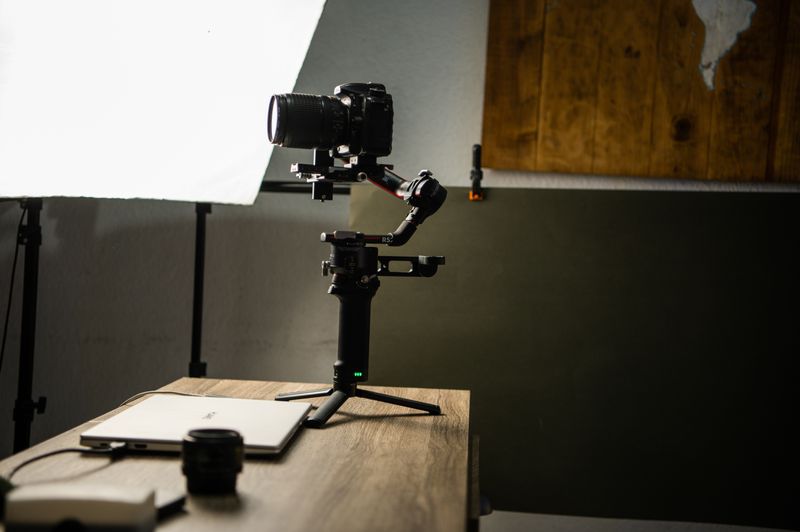 Gimbal e estabilizador para celular: quando compensam DSLR camera on gimbal setup in a well-lit photography studio with wooden accents.