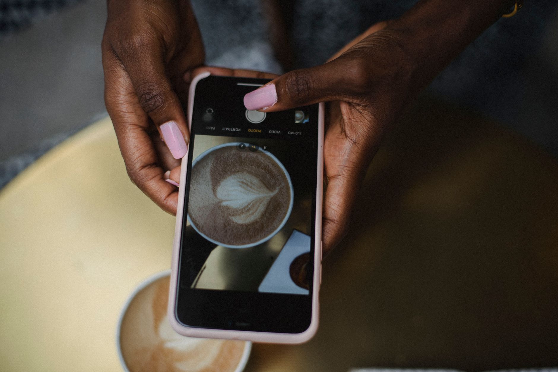 iPhone 16e x iPhone 16: o que você perde economizando A person photographing a latte with unique art using a smartphone.