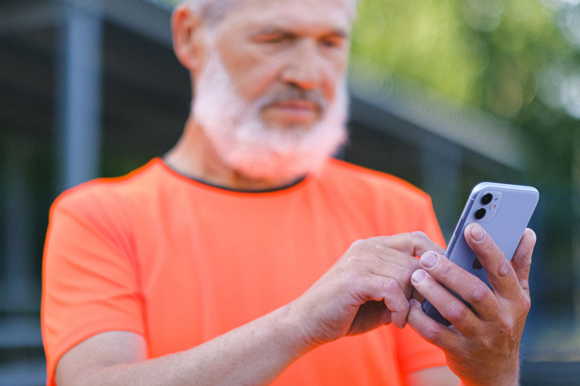 Como escolher entre iPhone SE e iPhone 16e Crop mature gray haired male with beard browsing mobile phone while spending time in city park