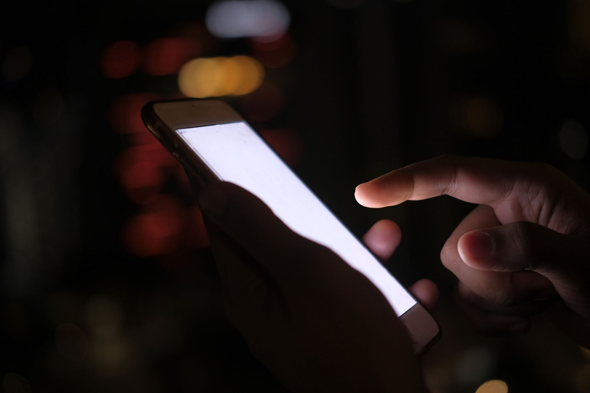 Como escolher entre leitor de digital na tela ou lateral Close-up of a hand using a smartphone in the dark with blurred city lights in the background.
