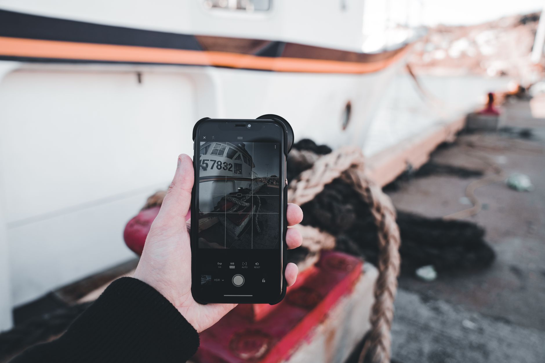 Moto G x Galaxy A: qual linha intermediária vale mais? A person photographing a moored ship with a smartphone, emphasizing technology and travel.