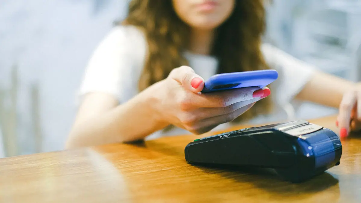 Mulher pagando com o celular em uma maquininha por aproximação