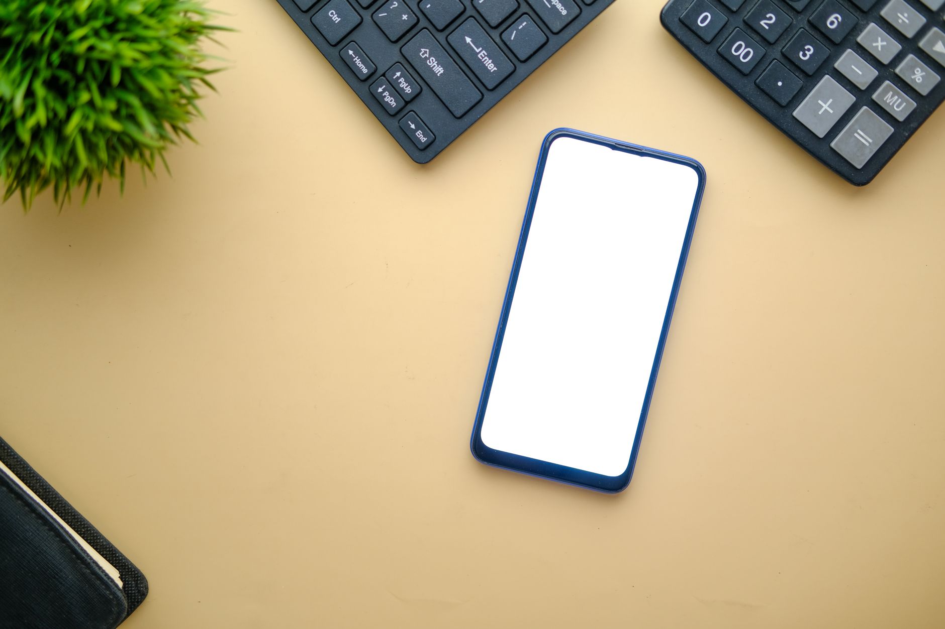 iOS 26: novidades e como saber se seu iPhone recebe A minimalist top view of a smartphone on a desk with keyboard and plant, perfect for mockups.