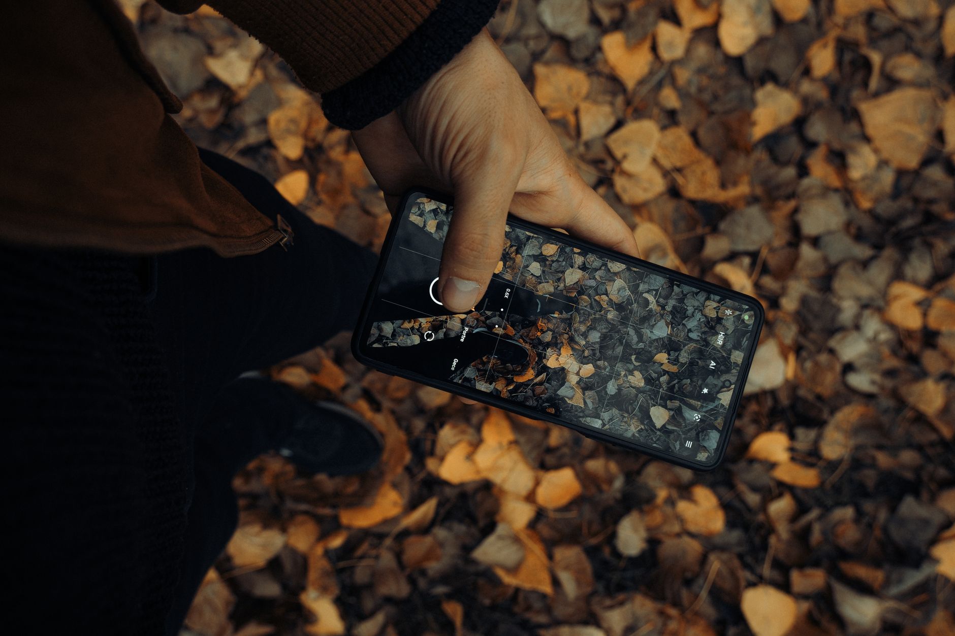 Mão segurando um smartphone moderno em ambiente externo com iluminação natural.