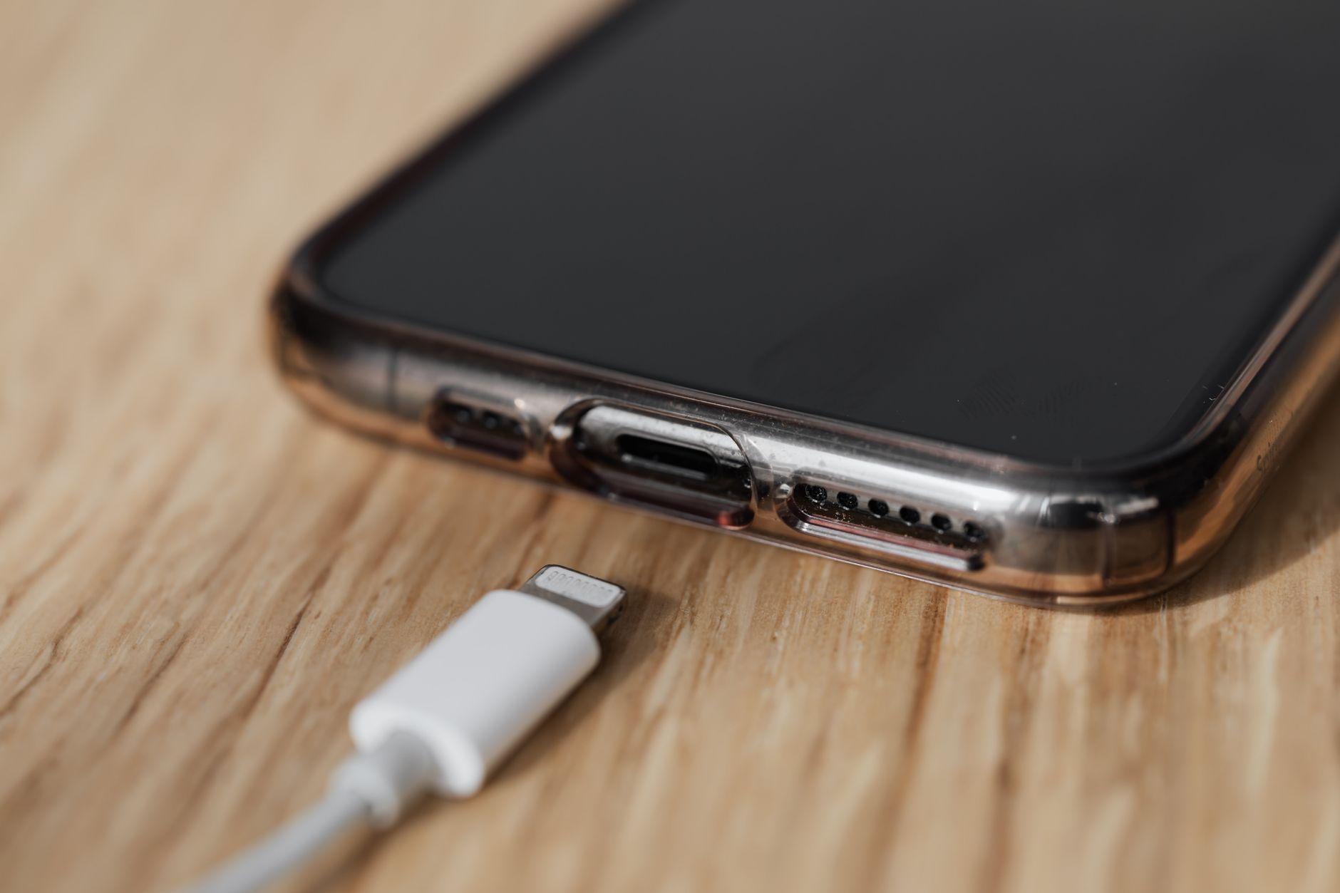 O que avaliar antes de comprar um celular dobrável em 2026 Modern cellphone in transparent cover with closeup of charging input and mobile phone white charger cable usb connector on wooden table