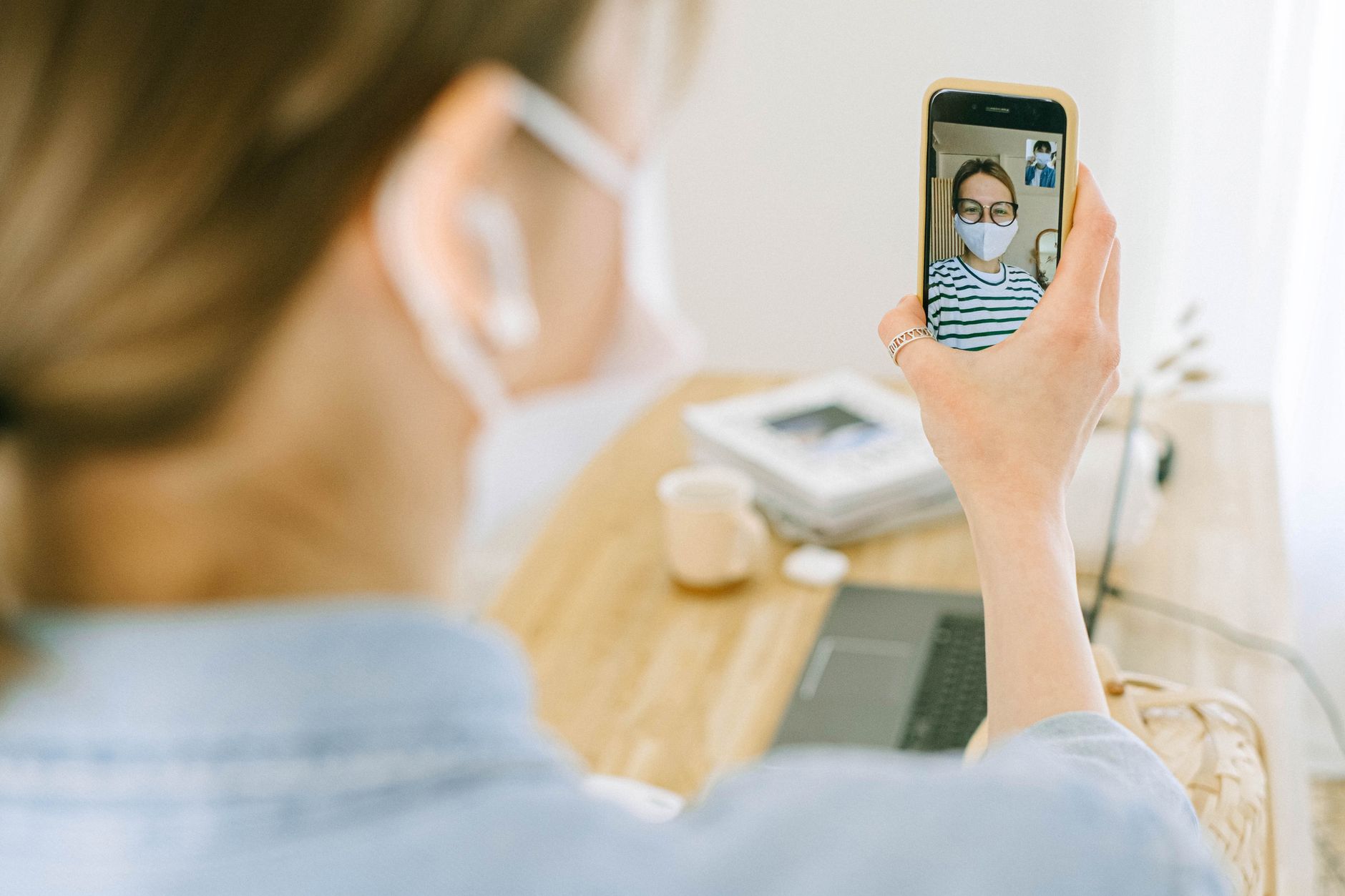 Woman wearing face mask making a video call on smartphone in cozy home setting.