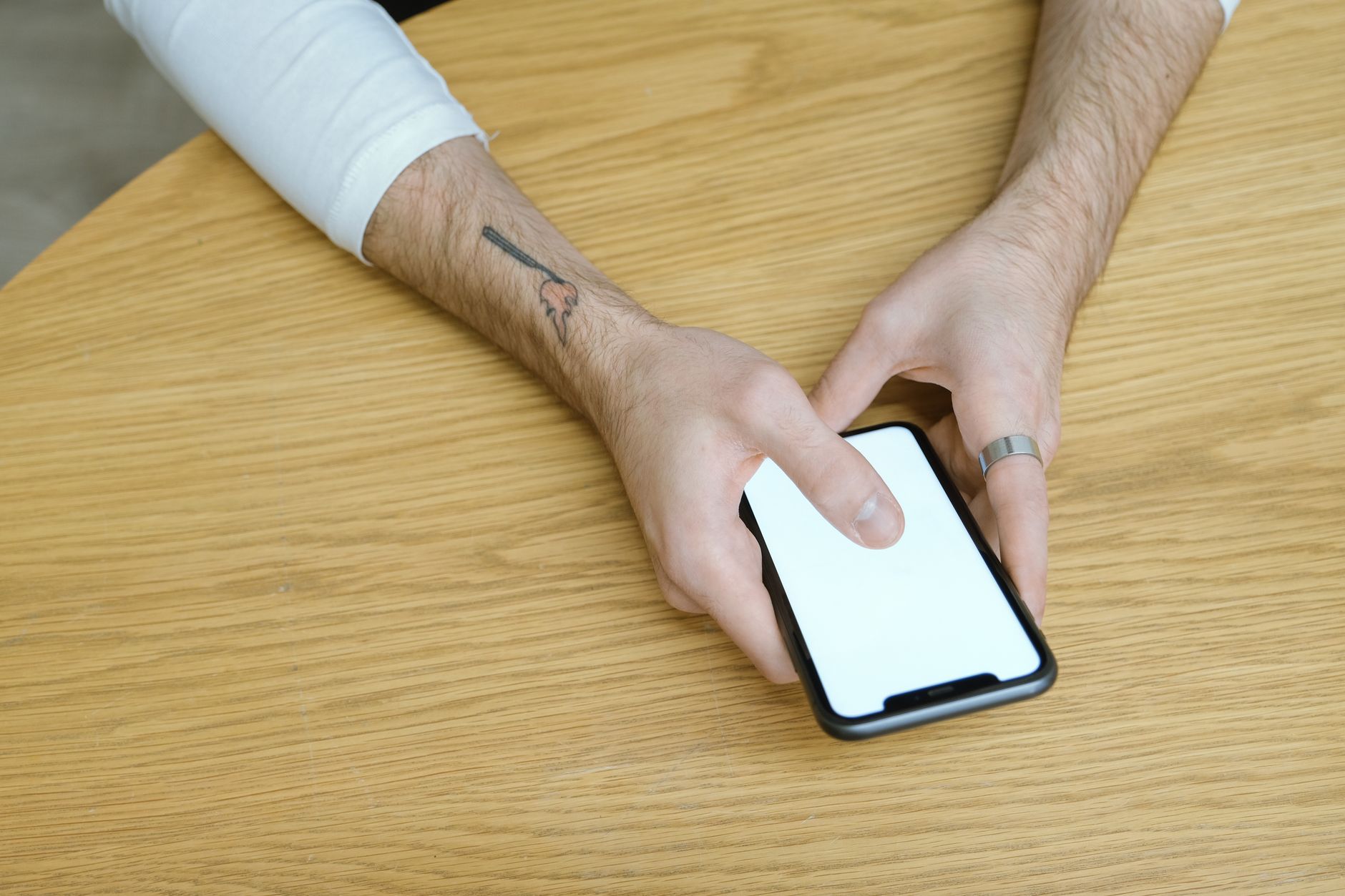 Onde vender seu celular usado com segurança Close-up of hands using a smartphone with a blank screen on a wooden table indoors.