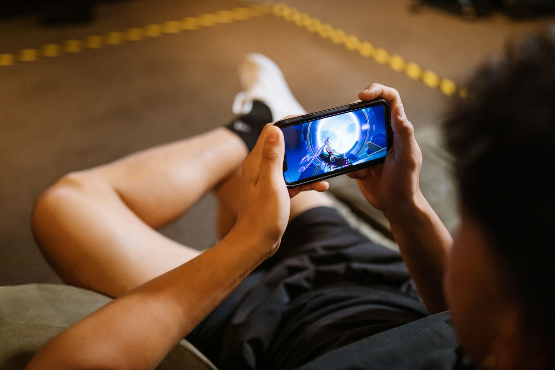 POCO X7 ou Moto G: desempenho ou experiência? Man playing a video game on a smartphone while sitting comfortably indoors.