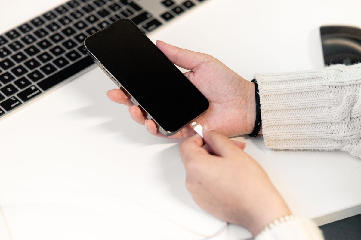 Pessoa segura um smartphone com a entrada USB-C virada para cima sob luz para inspecionar o conector.