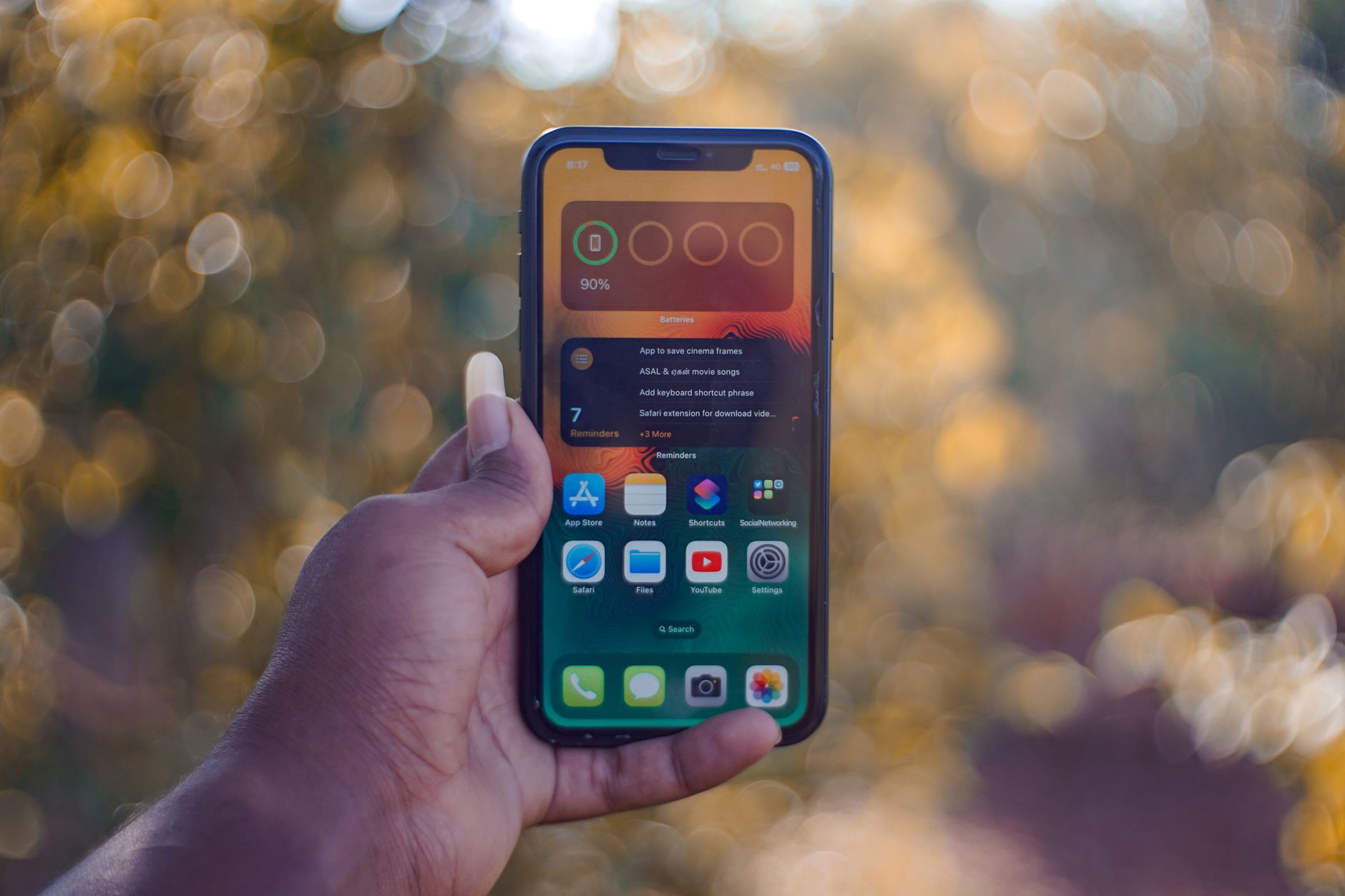 Quanto de RAM você realmente precisa no celular em 2026 Image of a person's hand holding a smartphone against an outdoor bokeh background.