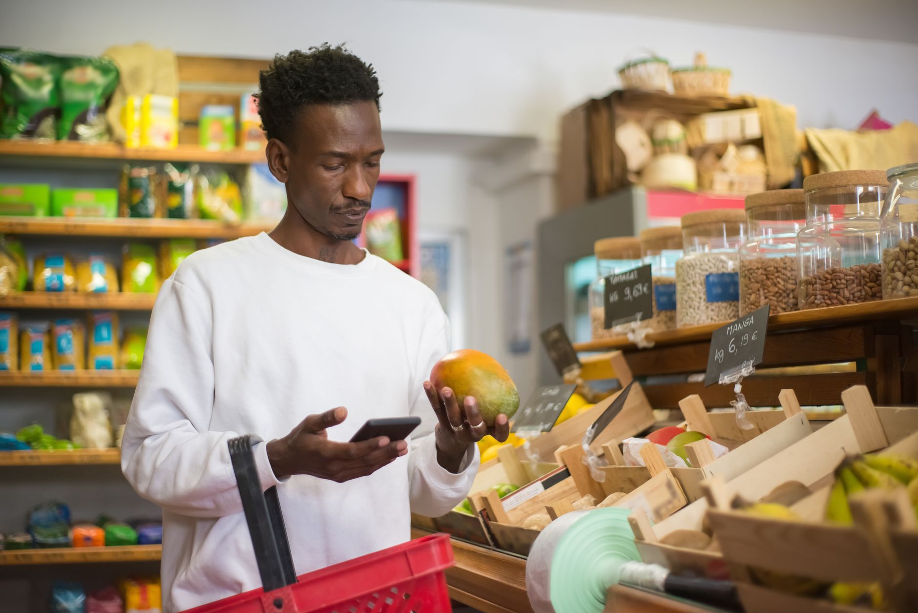 Como escolher entre realme e Xiaomi no Brasil A man examines a mango while shopping with a smartphone in a grocery store.