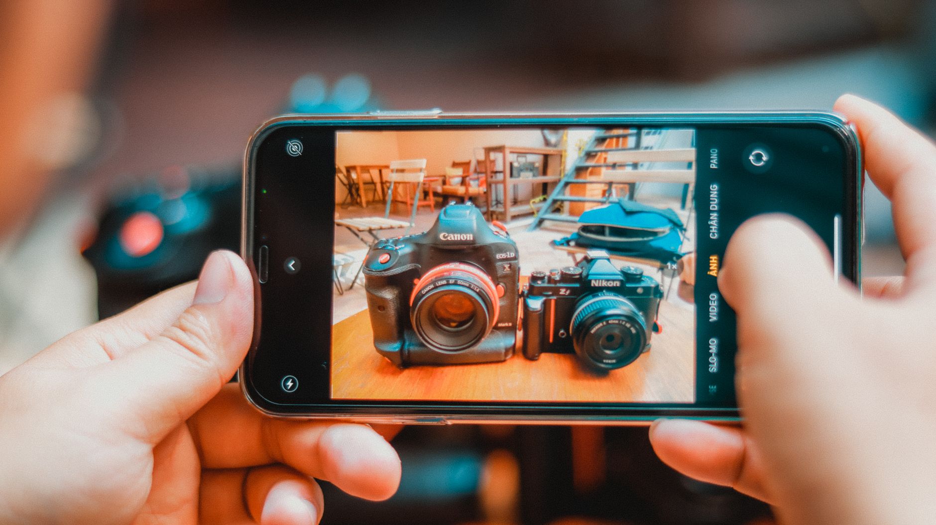Galaxy A36: análise completa antes de comprar Person photographing DSLR and vintage cameras with smartphone indoors.